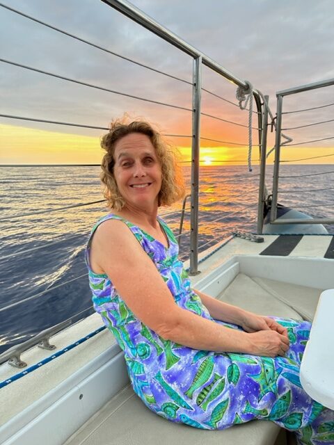 Photo of Cathy Whitaker sitting on a boat on the ocean at sunset.